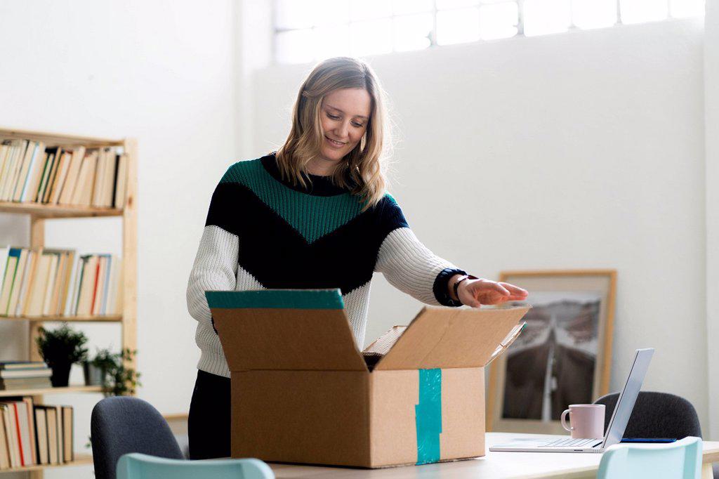 Mid adult woman opening cardboard box at home