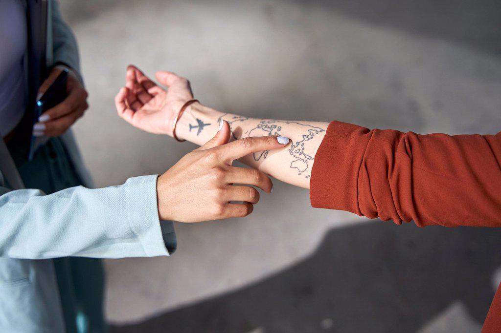 Businesswoman pointing at tattooed world map on hand of female colleague
