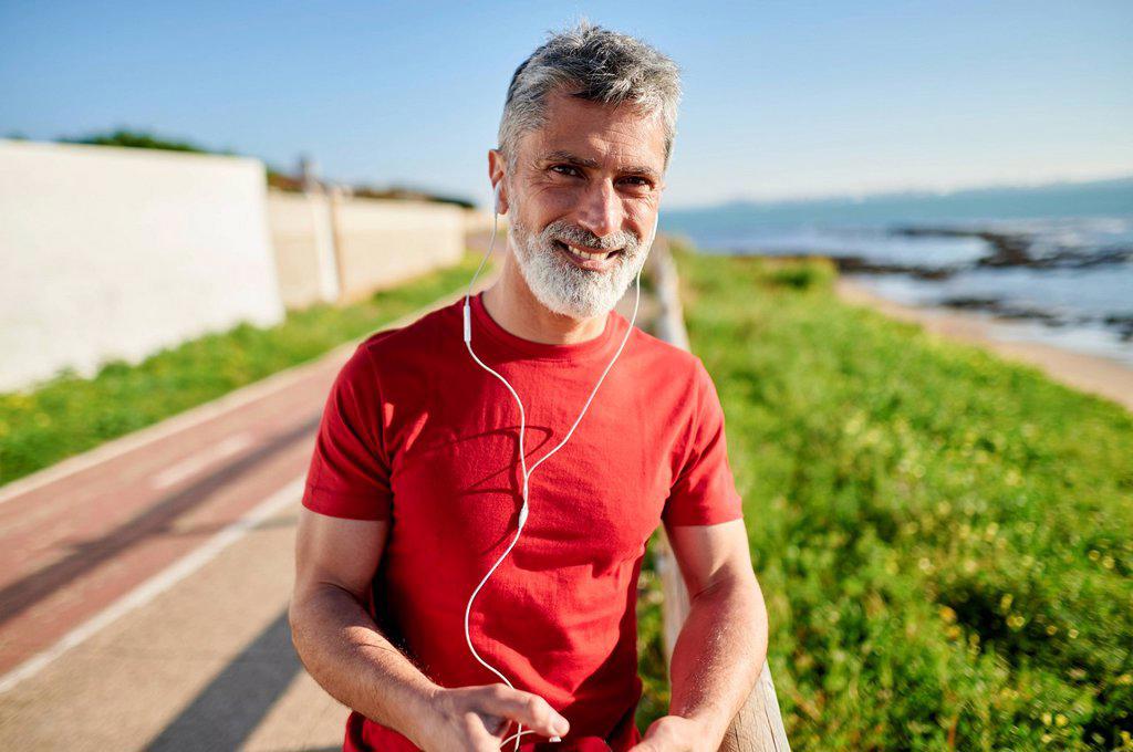 Smiling man with earphones leaning on railing by the sea