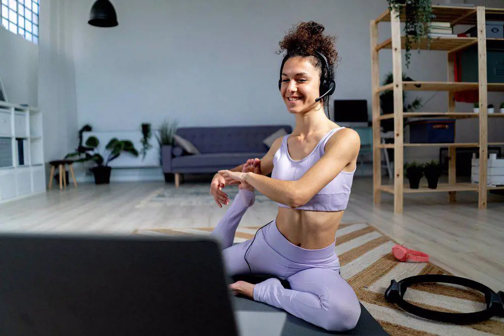Smiling yoga influencer with headphones doing mermaid pose while vlogging through laptop at home