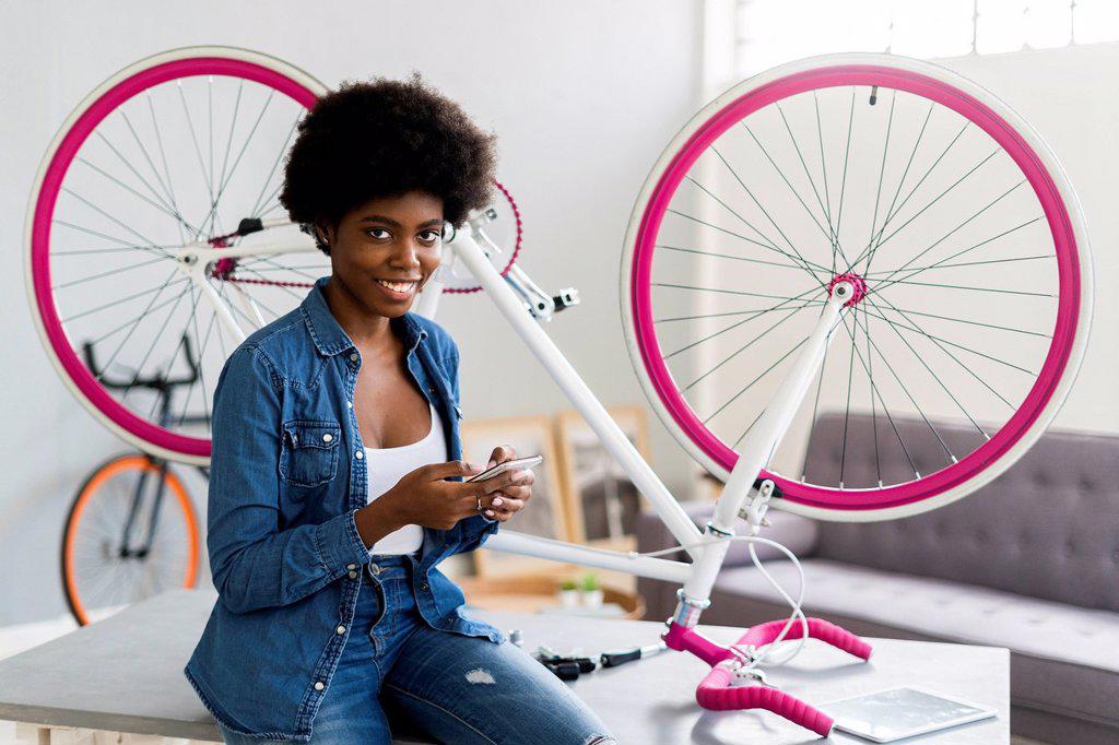 Smiling young woman using mobile phone by upside down cycle on table at home
