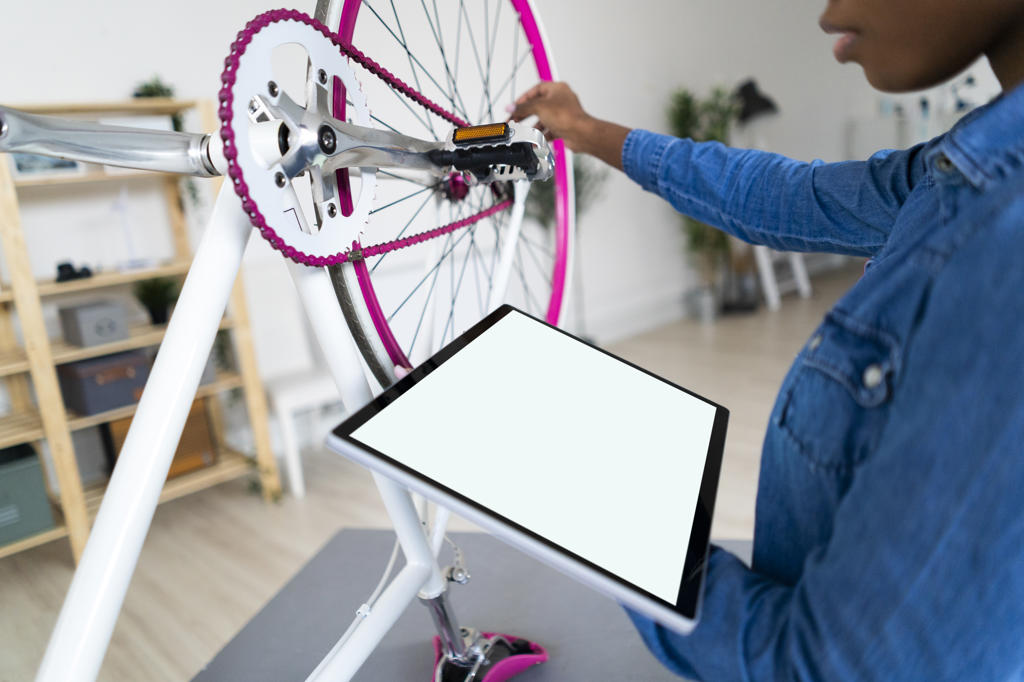 Young woman with digital tablet repairing bicycle at home