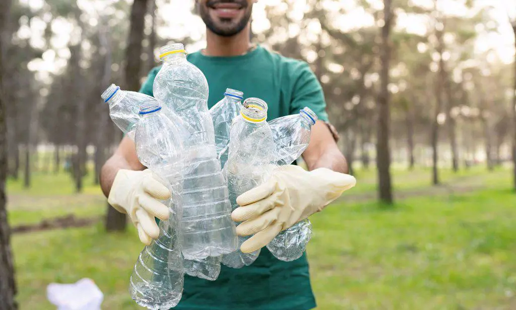 Male volunteer holding plastic bottles while cleaning forest