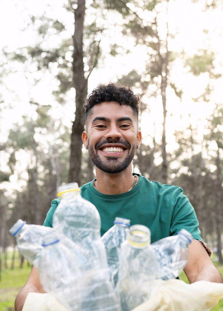 Smiling young male volunteer collecting plastic bottles in forest