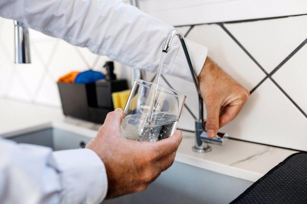 Male professional filling glass with water through tap at home