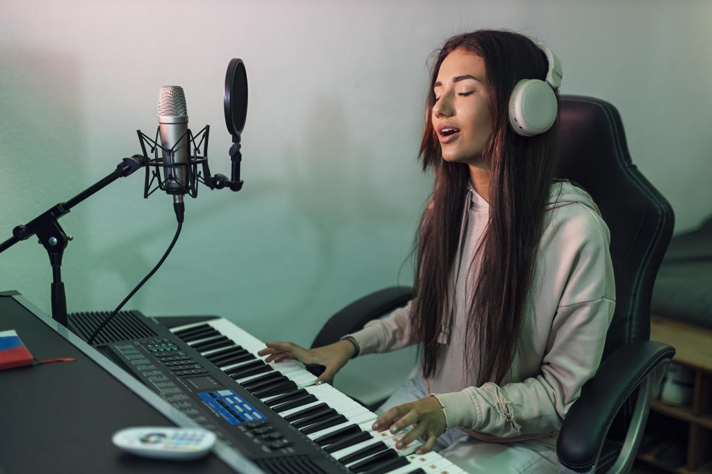 Young female singer singing while playing piano in studio