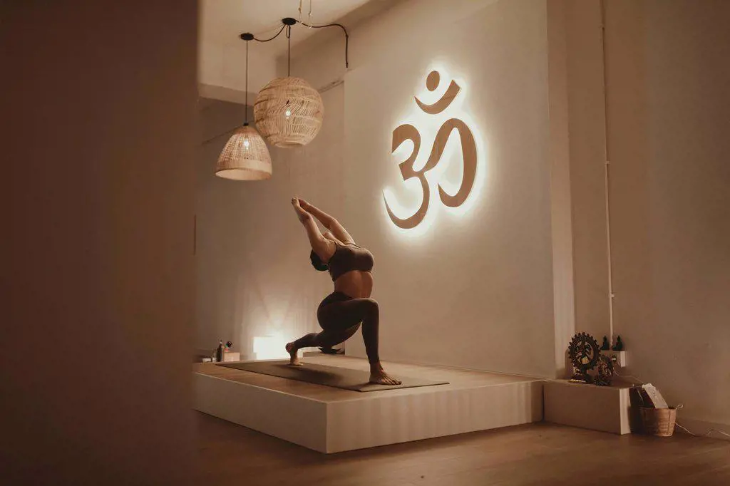 Female yoga instructor with arms raised bending while practicing by Om symbol