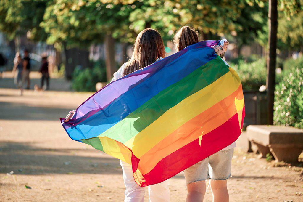 Lesbian couple holding rainbow flag while walking at park