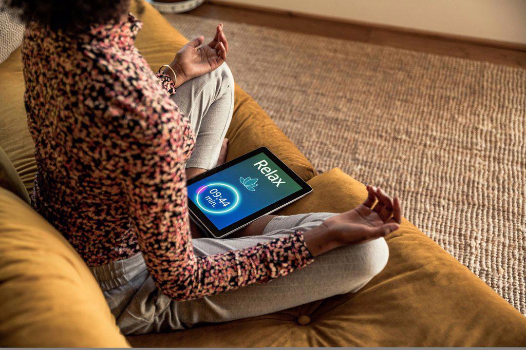 Young woman doing yoga while sitting with digital tablet on sofa