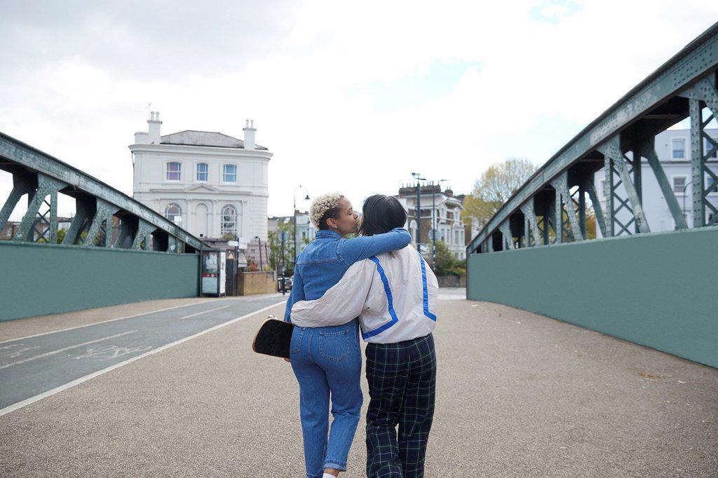 Lesbian woman with arm around kissing girlfriend walking on bridge