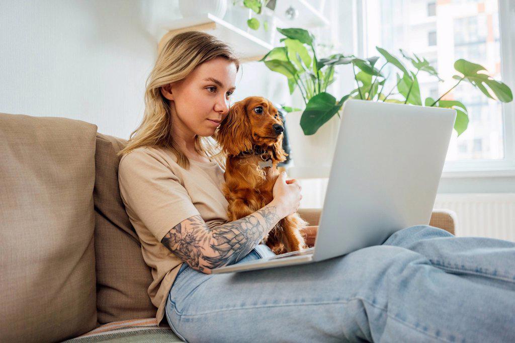 Female professional sitting with dog while working on laptop at home