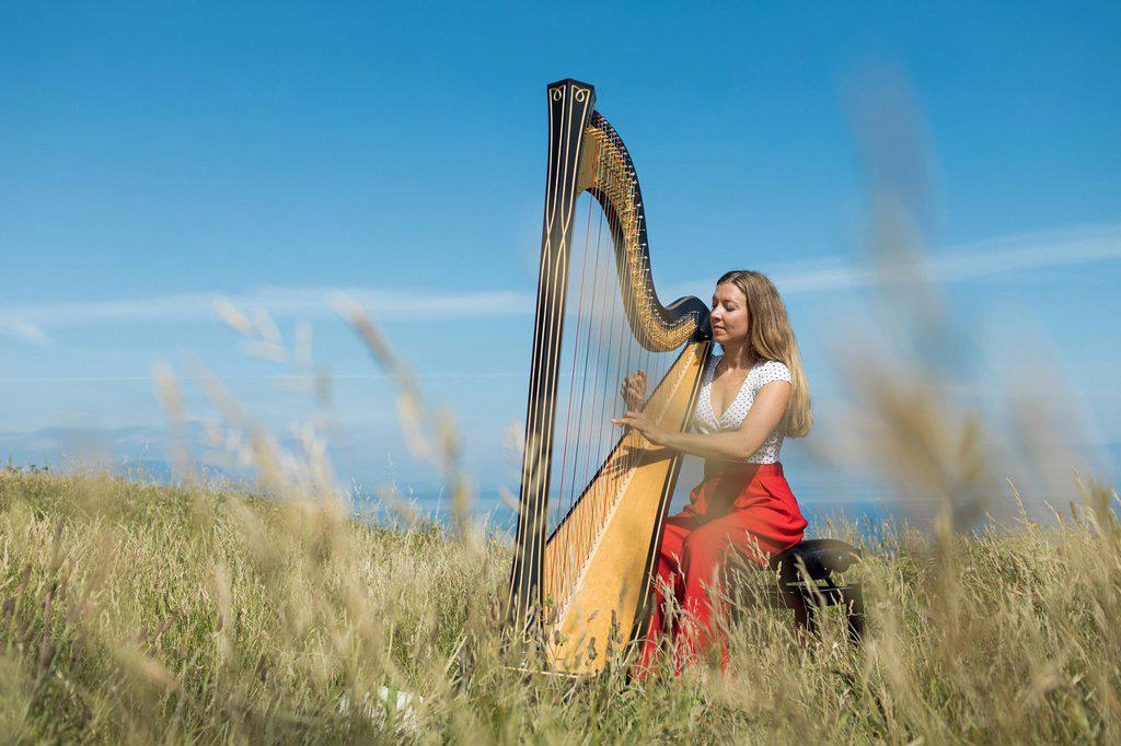 Young female musician practicing harp in meadow during sunny day