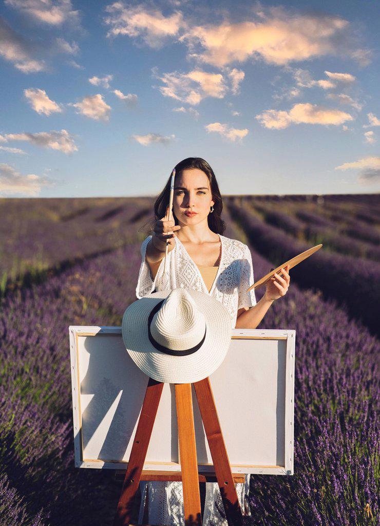 Young woman with canvas and paintbrush in lavender field