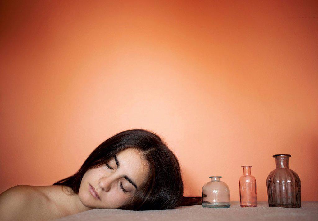 Topless young woman resting head on table by vases in front of orange background