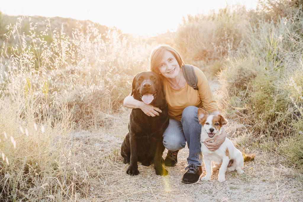 Woman embracing dogs while crouching on trail