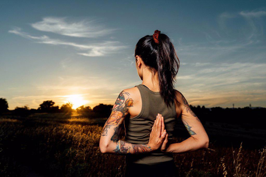 Woman with hands clasped behind back practicing yoga at countryside