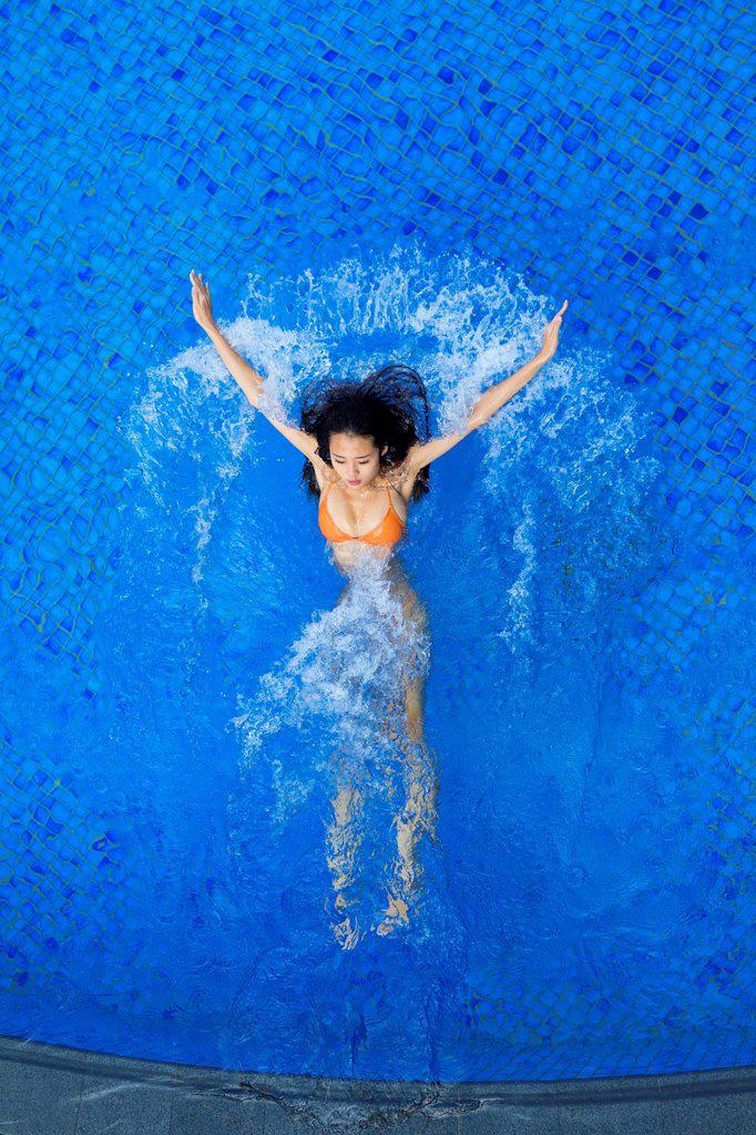 Young woman splashing water while swimming in pool