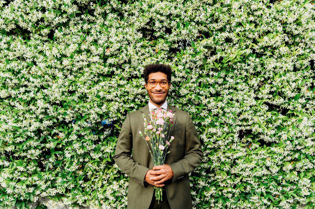 Happy businessman holding bouquet while standing in front of flowering plant