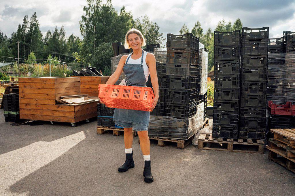 Smiling female agriculture worker carrying crate while standing on footpath