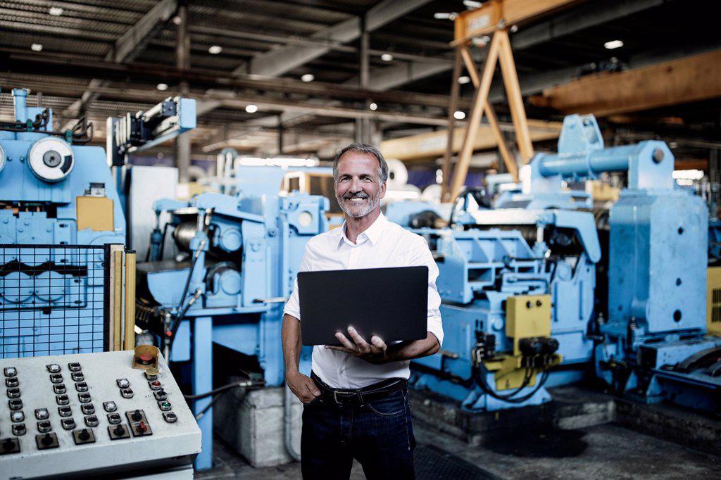 Smiling male professional holding laptop at steel mil