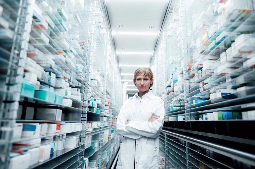 Confident female pharmacist with arms crossed standing amidst racks at medical store