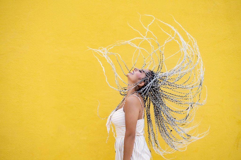 Young woman tossing hair by yellow wall