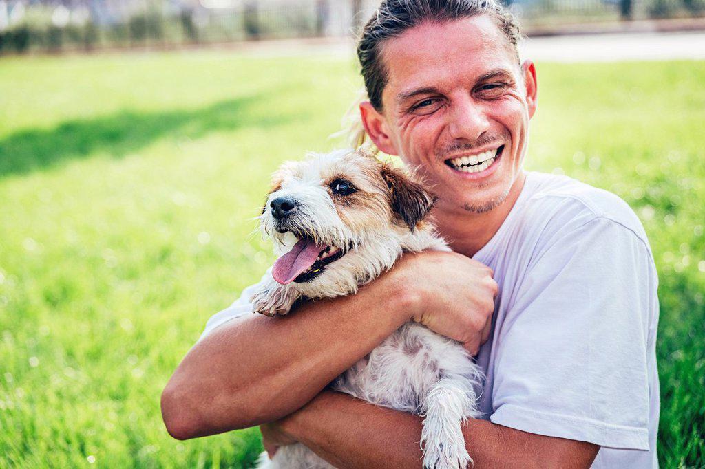 Mid adult man laughing while sitting with pet dog at lawn