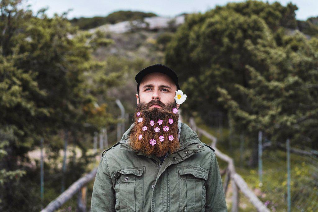 Young man wearing flowers in beard standing on bridge