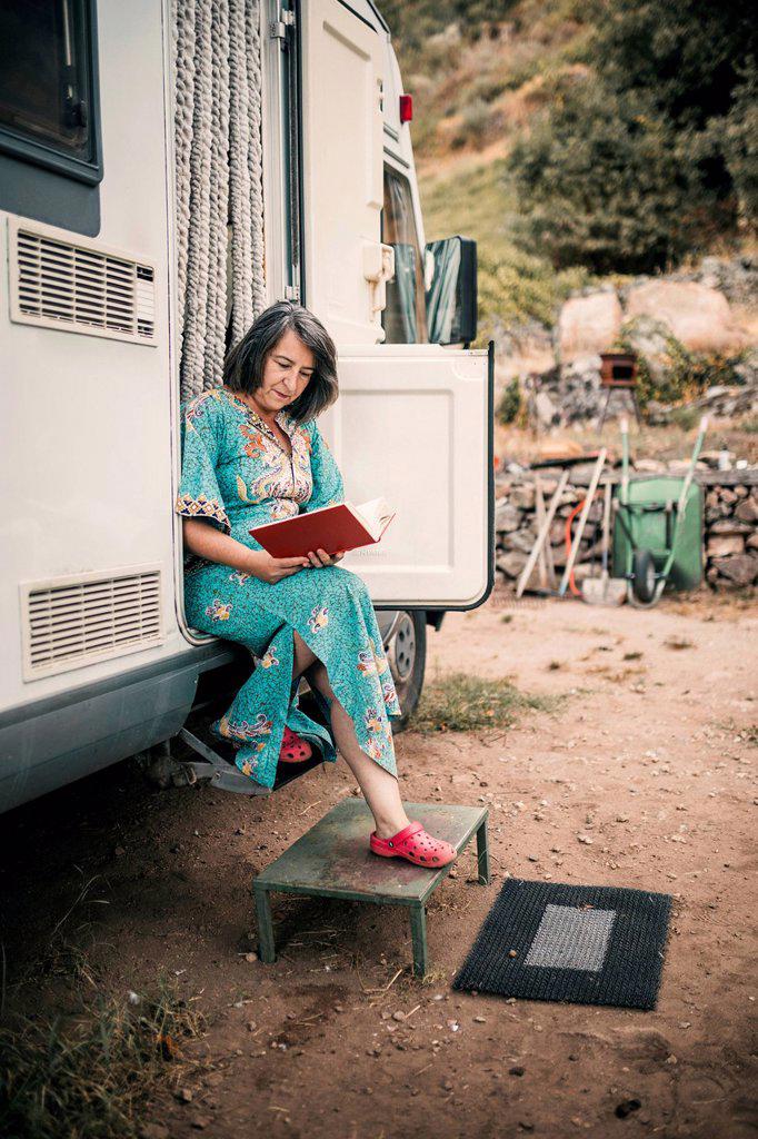 Woman reading book while sitting at camping van doorway
