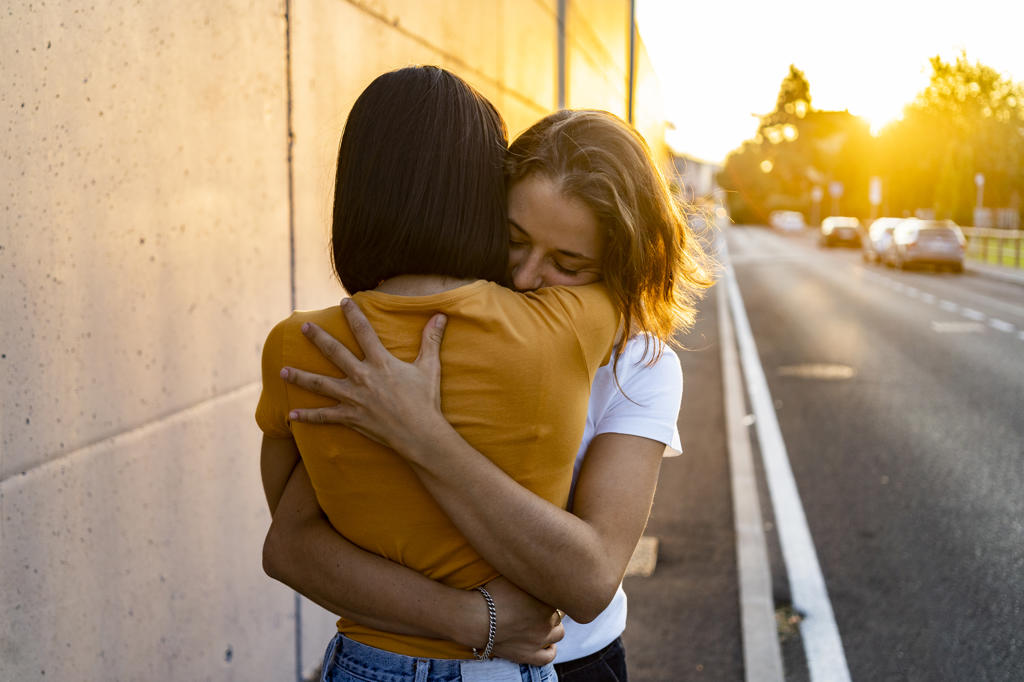 Woman hugging girlfriend on road during sunset