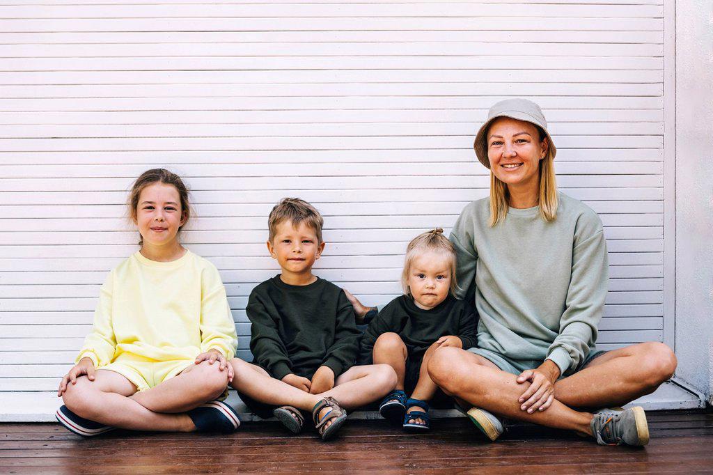 Smiling mother with sons and daughter sitting in front of shutter