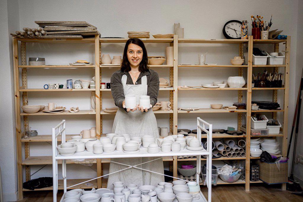 Smiling female potter showing ceramics in workshop