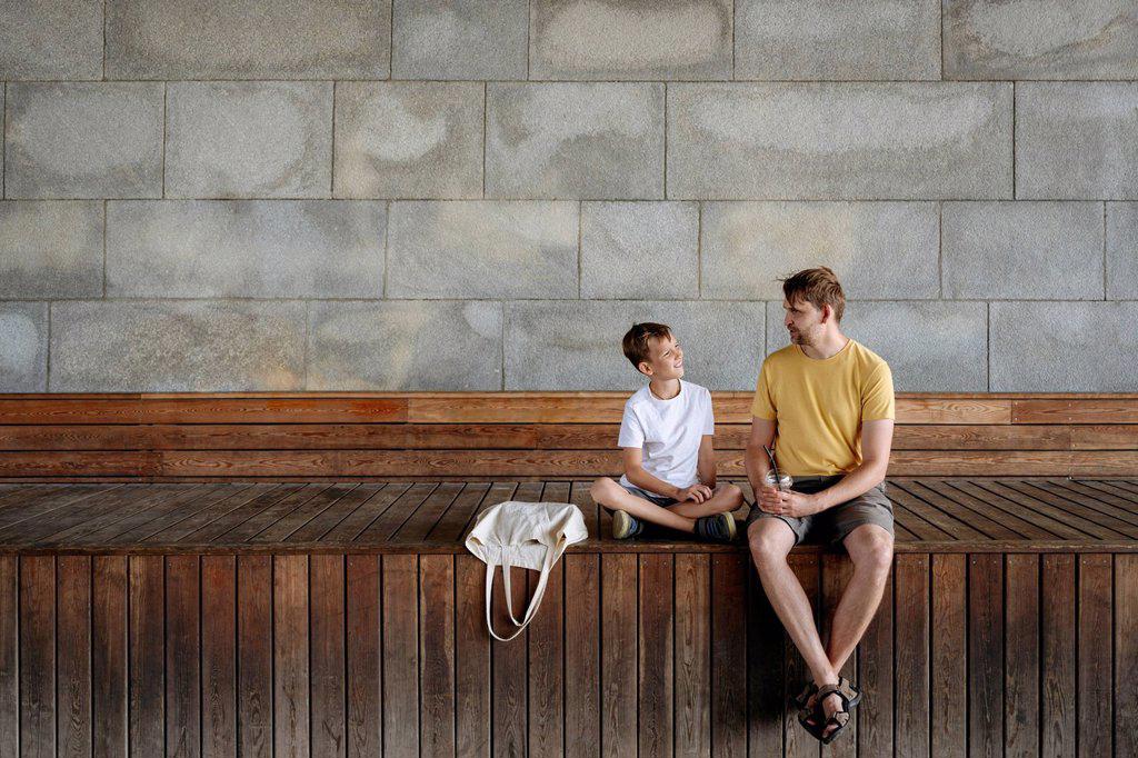 Boy talking with father while sitting on bench