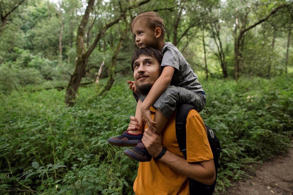 Man with backpack carrying boy on shoulders in forest