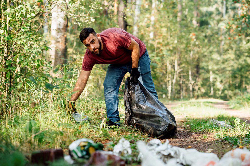 Mid adult male environmentalist collecting garbage in forest