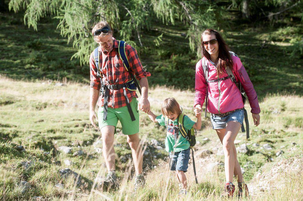 Happy parents holding hands of son while hiking on alpine meadow during vacation