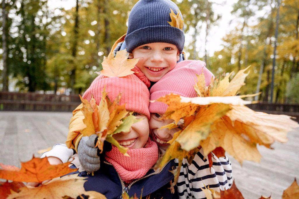 Smiling siblings playing with dry leaf during autumn