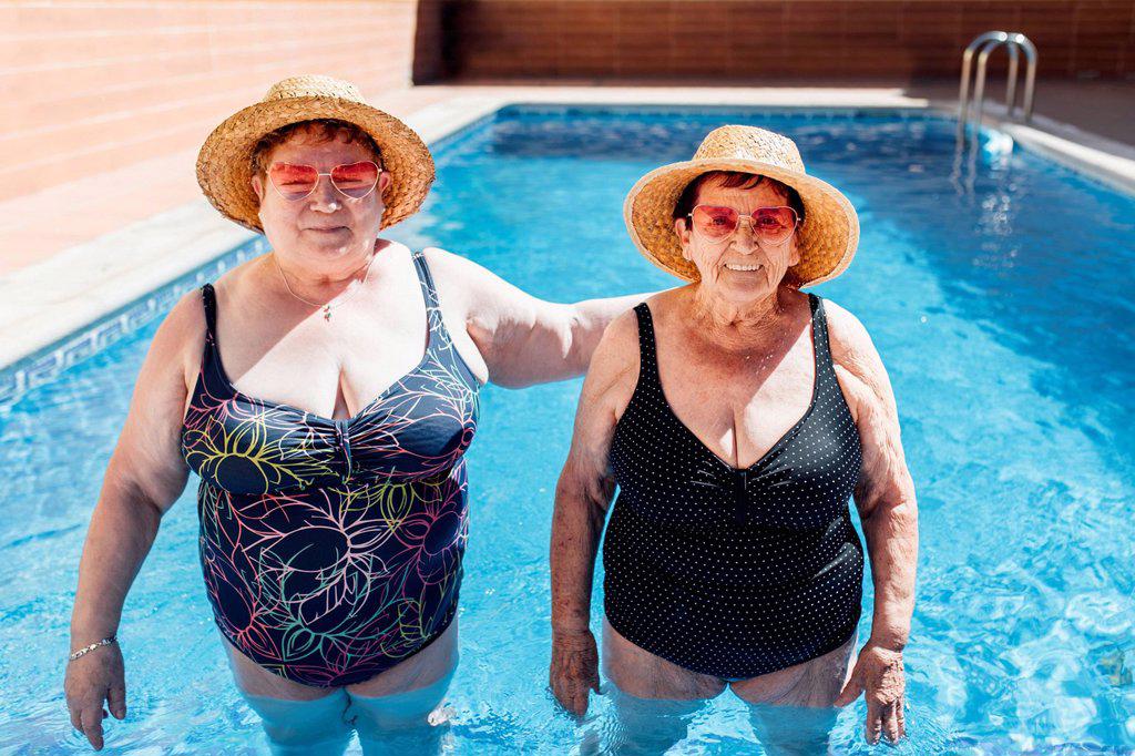 Female friends wearing sun hat standing in swimming pool during vacation