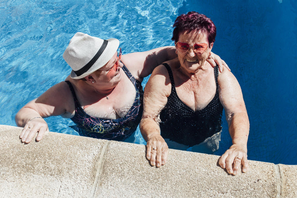 Happy woman wearing hat talking with female friend in pool