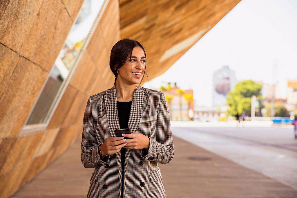 Smiling businesswoman holding smart phone on footpath