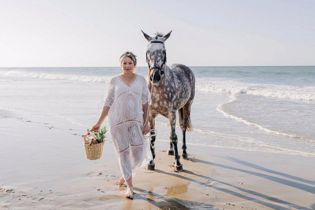 Pregnant woman with horse walking at beach on sunny day