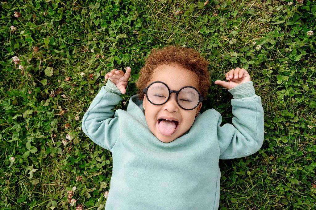 Cute girl with eyeglasses sticking out tongue on grass
