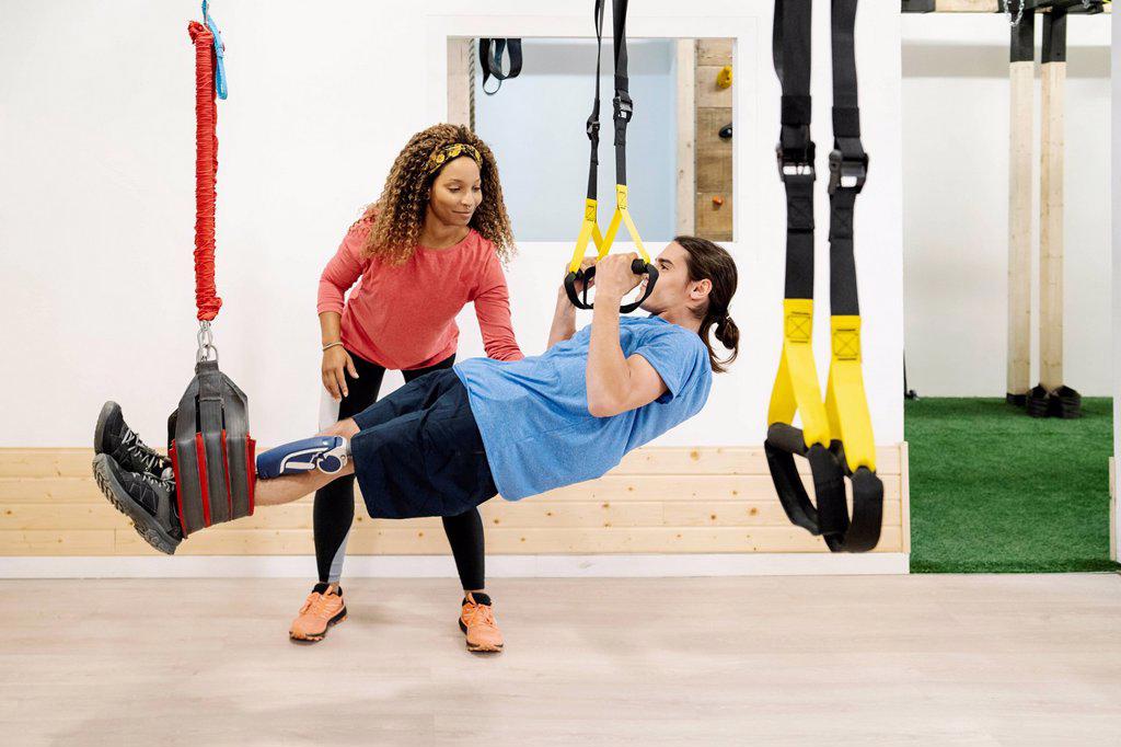 Smiling female instructor assisting disabled man exercising at gym