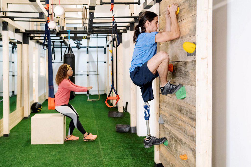 Disabled sportsman climbing wall in gym