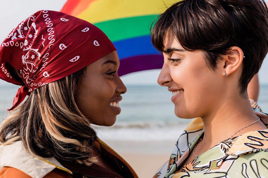 Romantic lesbian couple with rainbow flag staring each other at beach