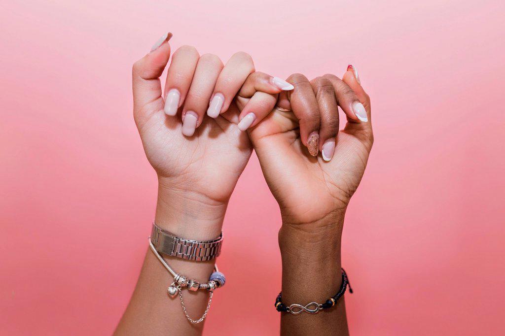 Lesbian couple making pinky promise against pink background
