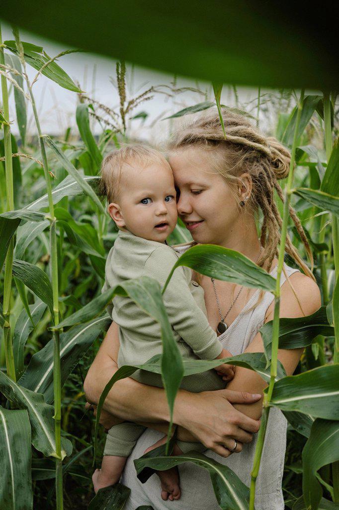 Mother with eyes closed embracing toddler in corn field