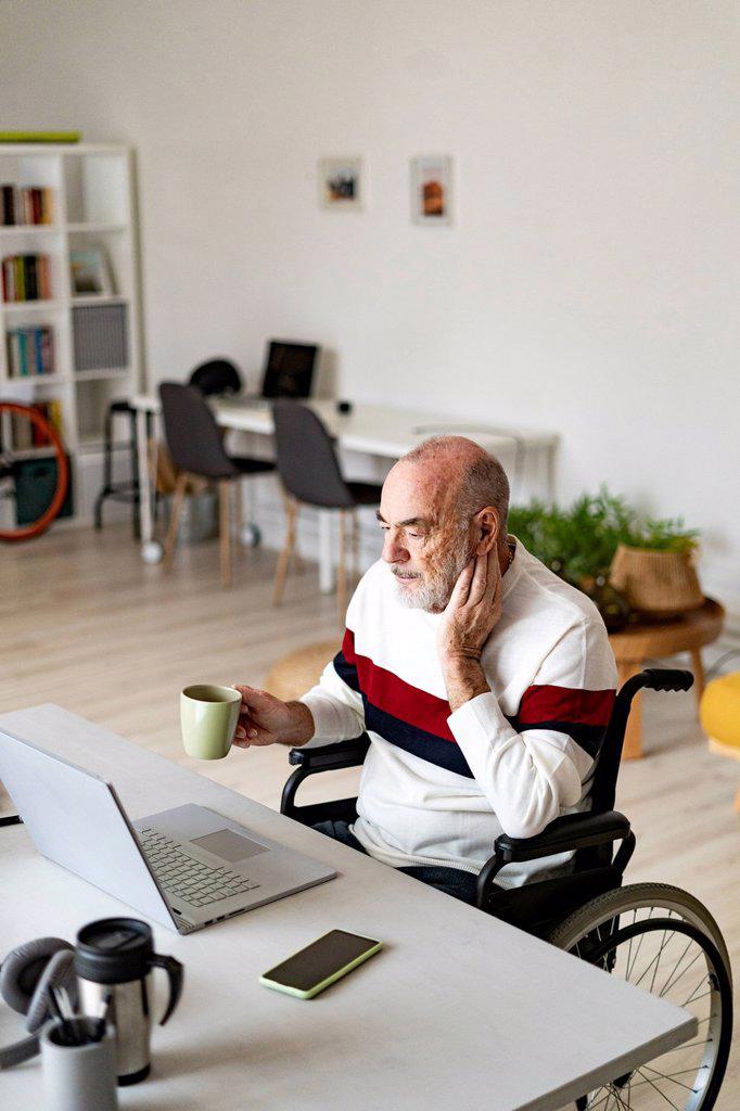 Senior freelancer on wheelchair holding coffee cup at home office