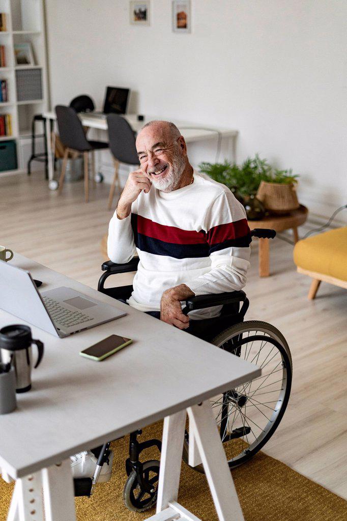 Smiling senior businessman sitting on wheelchair at home office