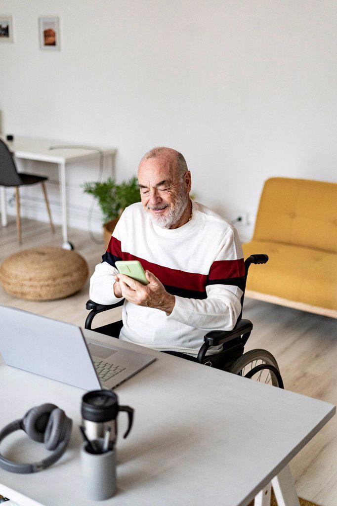 Senior businessman on wheelchair using mobile phone at home office